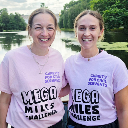 Photo of two Charity for Civil Servants staff members wearing pink Mega Miles tshirts standing in front of a lake