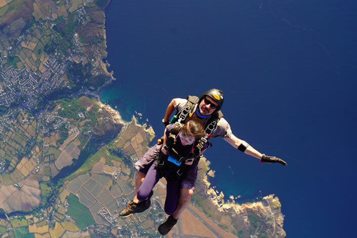 Photo of Stephanie and the skydive instructor having just left the plain with the land and sea below her