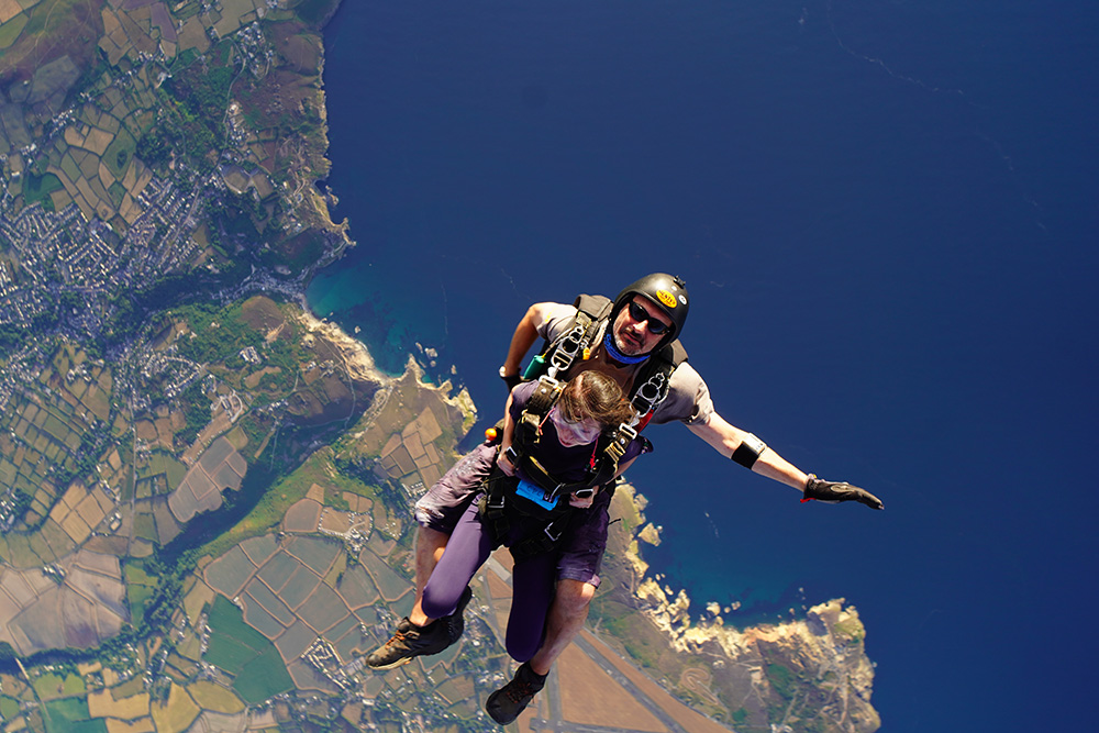 Photo of Stephanie and the skydive instructor having just left the plain with the land and sea below her