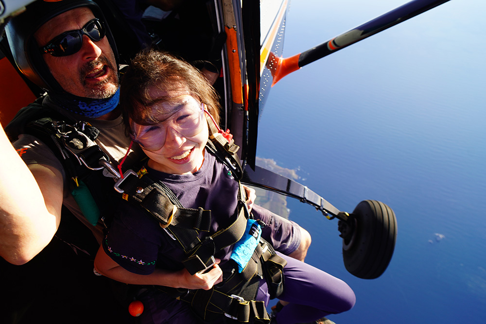 Photo of Stephanie attached to her skydive instructor sitting on the edge of the plane ready to begin her skydive