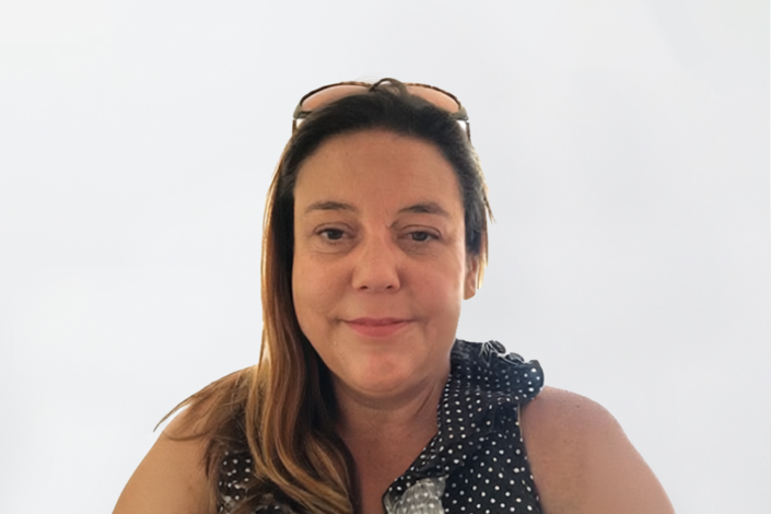 Photo of Lorna with long light brown hair with sunglasses on the top of her head and wearing a navy and white polka dot sleeveless top