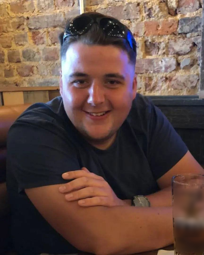 Photo of Sean in his twenties wearing a navy tshirt with his arms crossed in front of him