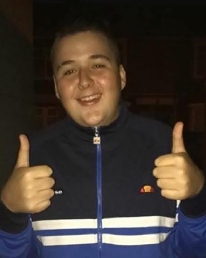Photo of Sean aged about 15 with his thumbs up wearing a navy, blue and white sports zipped jacket